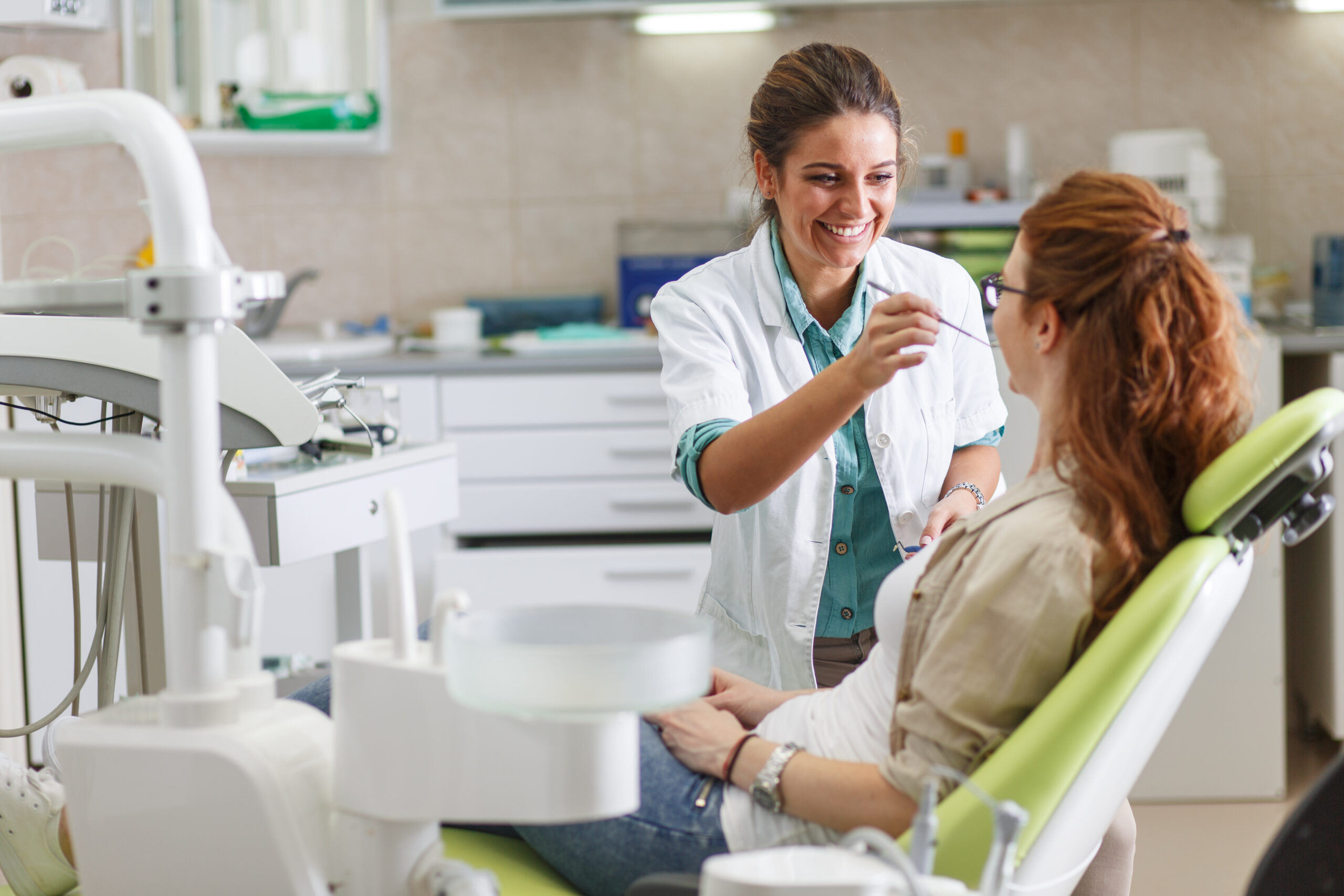 dentist helping a patient that is laying down in a green dental chair